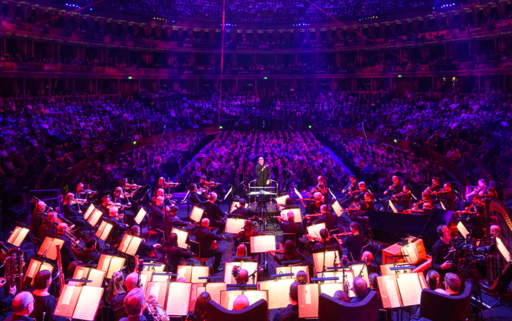 Orchestra performing with a full audience filling the Royal Albert Hall auditorium in the background