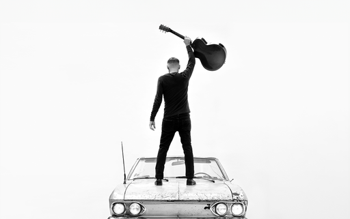 Bryan Adams standing on a car with a guitar in his hand