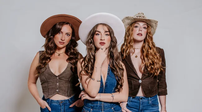Three women in double denim and cowboy hats face the camera.