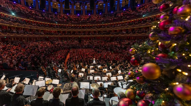 John Rutter conducting an orchestra with a Christmas tree in the foreground