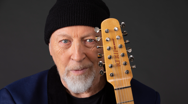 Close up on Richard Thompson's face with the top of his guitar pressed to his head