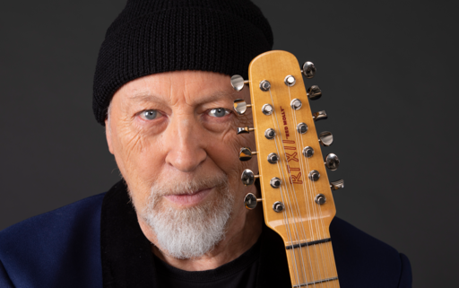 Close up on Richard Thompson's face with the top of his guitar pressed to his head